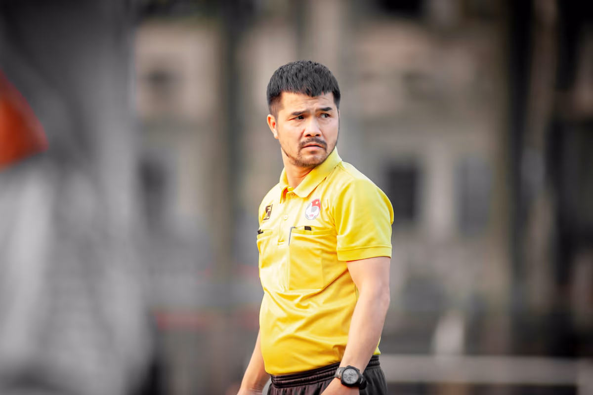 โค้ชฟุตบอลเสื้อเหลืองยืนจดจ่อมองเกมอยู่ข้างสนาม