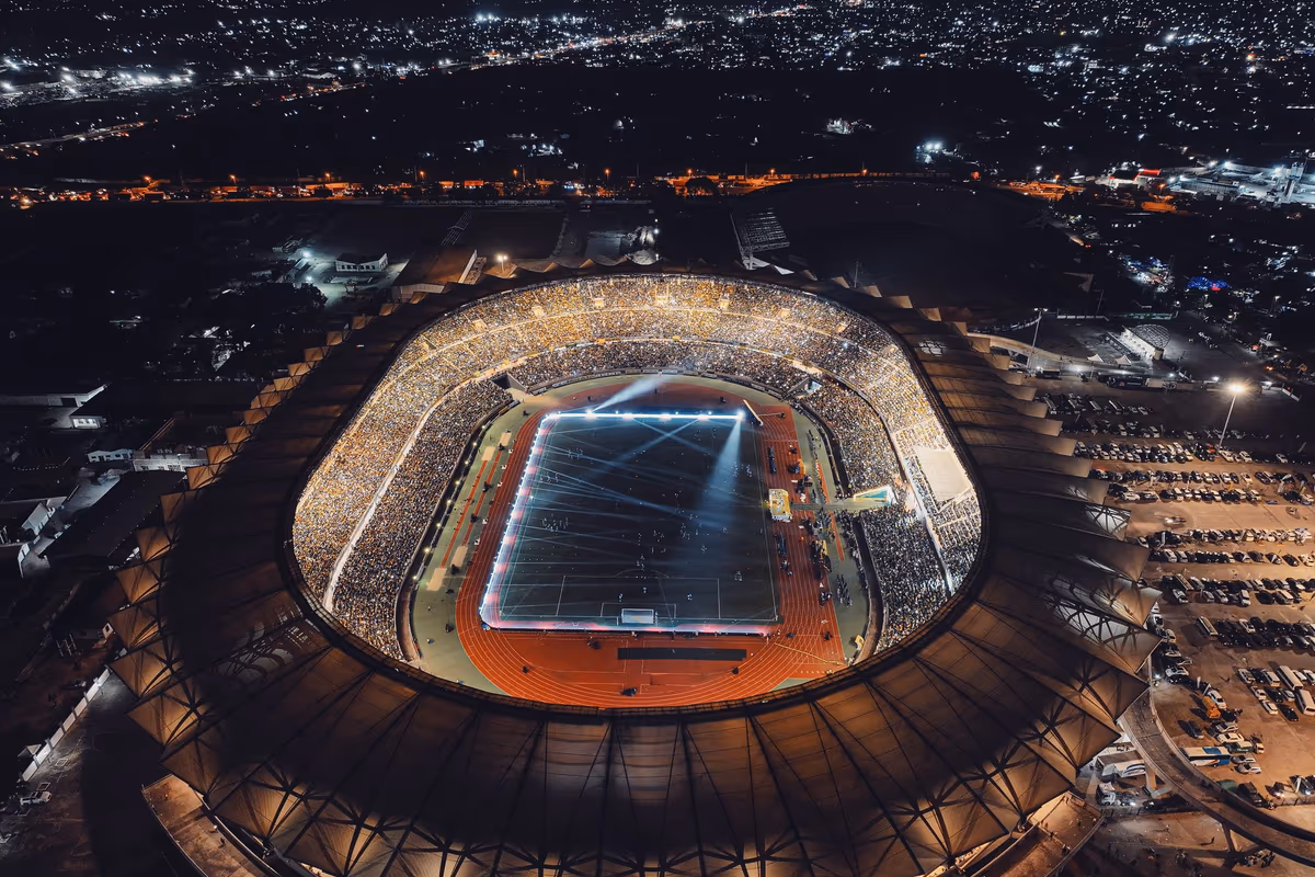 ภาพมุมสูงของสนามฟุตบอลที่สว่างไสวด้วยไฟสปอตไลต์เต็มความจุยามค่ำคืน